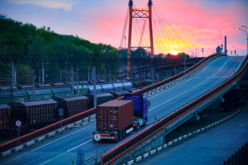 truck with container rides on the road, railroad transportation, freight cars in industrial seaport at sunset