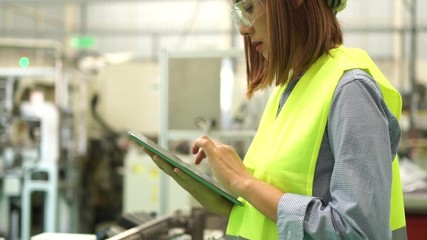 Poster - Asian  engineer wearing a Yellow safety helmet.while working with a Tablet for Machine inspection in the factory , the expression is serious face.