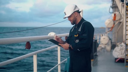 Wall Mural - Marine chief officer or chief mate on deck of ship or vessel. He fills up ahts vessel checklist. Ship routine paperwork. He holds VHF walkie-talkie radio in hands.