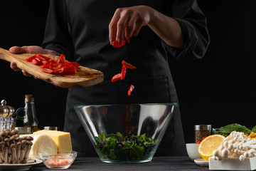 Wall Mural - The cook pours cherry tomatoes into a bowl with salad,. Salad, organic ingredients and products. Vegetarian and tasty food. Advertising photo of food, on a black background