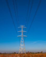 Electric pole and electric cable on the field in the countryside with blue sky.