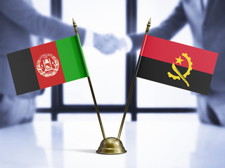 Angola and Afghanistan mini table flags on white wooden desk. Diplomatic background with men shaking hands, international relations and agreements.