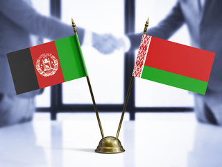 Belarus and Afghanistan mini table flags on white wooden desk. Diplomatic background with men shaking hands, international relations and agreements.