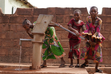 three eager little african girls trying out their village water pumping station