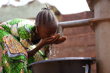 nicely braided african girl washing her face with fresh water at the borehole