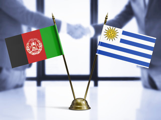 Wall Mural - Uruguay and Afghanistan mini table flags on white wooden desk. Diplomatic background with men shaking hands, international relations and agreements.