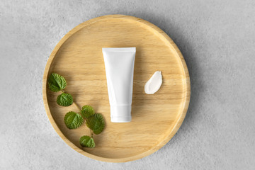 Top view of Organic gentle skincare tube with mint leaves and rich moisture butter cream smear on a wooden plate grey color as a background