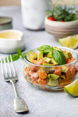 Wall Mural - Delicious avocado and raw salmon salad, tartare, served glass jar with lime, light background