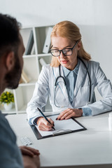 Wall Mural - selective focus of attractive doctor in glasses writing prescription near man