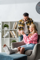 Wall Mural - handsome man giving cup of tea to injured woman at home