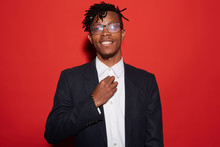 Waist Up Portrait Of Trendy African-American Man Smiling Cheerfully While Posing Against Red Background, Shot With Flash