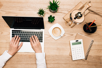 Poster - Top view of businesswoman using laptop by coffee and calculator on table, cropped view