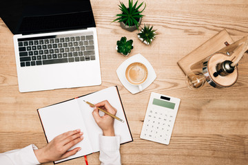 Poster - Top view of businesswoman writing in notebook by calculator, laptop and coffee on table