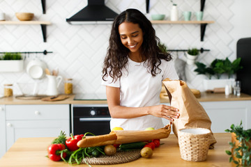 Smiled beautiful girl is putting packages with  food on the table on the modern kitchen