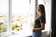 Young Woman Opening Window In Living Room At Home