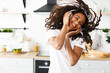 Smiled girl with curly hair in big wireless headphones is happily dancing with her eyes closed in the modern kitchen