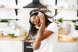 Smiled hilarious girl with messy hair in big wireless headphones is happily dancing with her opened mouth in the modern kitchen