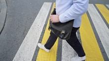 Top View Profile Side Shot Of Young Man No Face In A Blue Pants And White Sneakers, Leather Bag Crossing The City Road On Yellow White Crosswalk Alone
