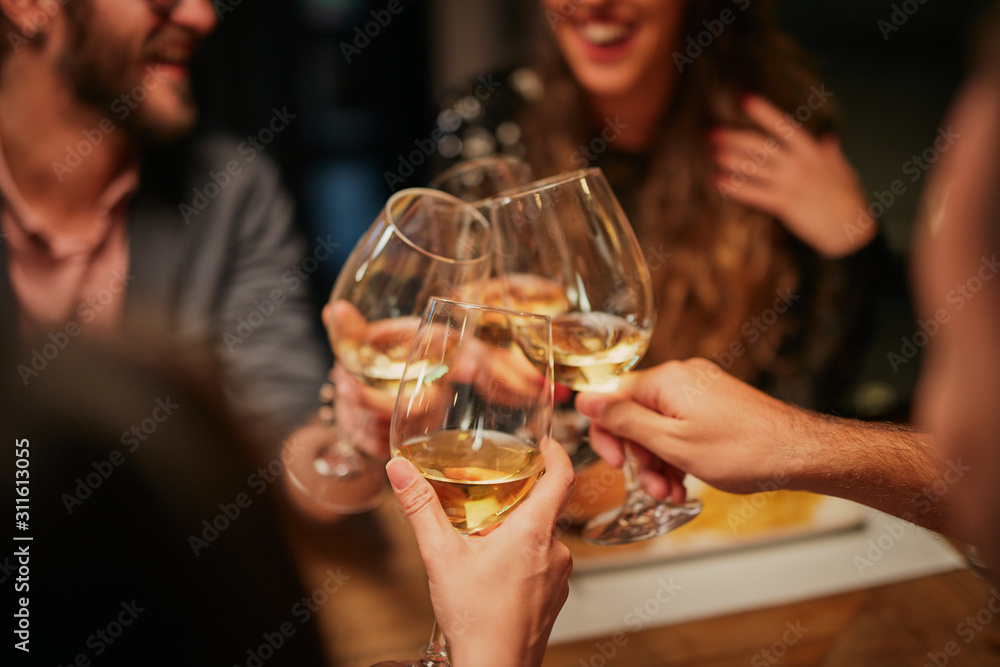 Best friends sitting in restaurant for dinner and making a toast with white wine. On table is food.