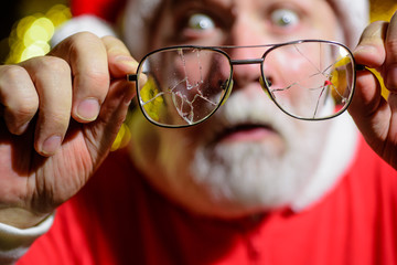 Wall Mural - Santa man with broken glasses. Selective focus. Eyeglasses with broken lens. Santa Claus holds cracked eyeglasses. Santa with broken eye glasses. Bearded man in Santa hat hold broken men's eyeglasses.