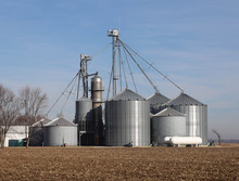 Grain Silos In The Field With A Blue Sky Background Along With A Grain Drier.