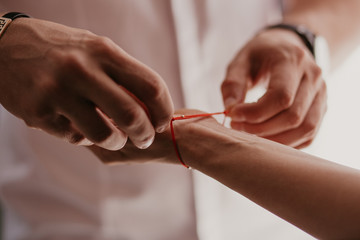 Man ties a red bracelet on woman's hand, red thread, jewelry, bracelet with a stone, women's accessories. Authentic love