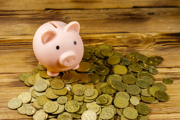 Pink piggy bank on a heap of coins on wooden background. Saving money concept