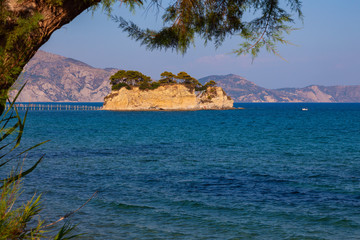 Wall Mural - Seascape - a small, picturesque island on a background of blue sea and clear sky. A pedestrian wooden bridge leads to the island. In the foreground is a tree