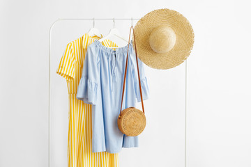 Wall Mural - Summer dresses and straw hat with bamboo bag on hanger on white background. Elegant fashion outfit. Spring wardrobe. Minimal concept.