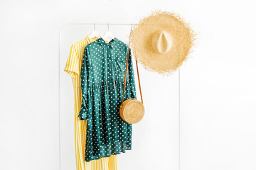 Wall Mural - Summer dresses and straw hat with bamboo bag on hanger on white background. Elegant fashion outfit. Spring wardrobe. Minimal concept.