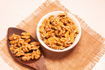 walnuts in bowl with jute cloth and wooden board background and spoon