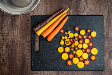 Wall Mural - Sliced rainbow carrots on a black cutting board, stainless-steel bowl, wood table