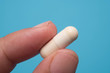 © kenary820 - Holding white tablet on blue background, macro shot. Health concept.