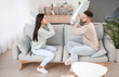 © Pixel-Shot - Young couple fighting on pillows while sitting on sofa at home