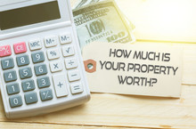 HOW MUCH IS YOUR PROPERTY WORTH? Words On Tag With Dollar Note And Calculator On Wood Backgroud,Finance Concept
