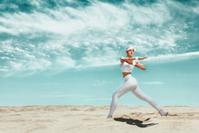 Sporty And Fit Young Woman Athlete Relaxed After Training At The Desert. Cloudy Day On Coast. The Concept Of A Healthy Lifestyle And Sport. Woman In White Sportswear.