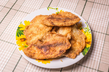 Fried tilapia fish fillets in plate on the kitchen table.