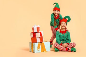 Sticker - Little children in costume of elf and with gifts on color background