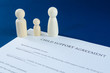 © lukecklukec - Printed child support agreement with man, woman and child wooden figures in a conceptual image for financial child support. Over blue background.