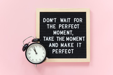 Wall Mural - Don't wait for the perfect moment, take the moment and make it perfect. Motivational quote on letter board, black alarm clock on pink background. Concept inspirational quote of the day