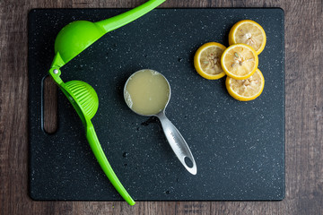 Wall Mural - Fresh squeezed lemon juice in measuring cup, citrus squeezer, lemons cut in half, black cutting board