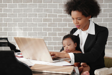 Wall Mural - african american mother holding her baby boy on hands while working with laptop computer at home