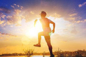Wall Mural - Silhouette of man trail run and jumping. Fit male fitness runner during outdoor workout with sunset background