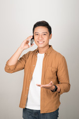 Wall Mural - Portrait of young Asian student listening to his phone call and standing isolated on white background