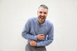 © Mangostar - Happy excited man laughing out loud, touching stomach. Grey haired young man in blue casual shirt posing isolated over white background. Fun or laughter concept