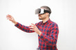 © Mangostar - Man in VR headset touching air. Serious bearded man in checkered shirt moving with hands and using VR headset on grey background. Technology concept