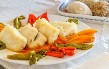 Wall Mural - Slices of hot fried cod fish with sweet bell pepper on the white dish and some bread buns on the table prepared for eating.