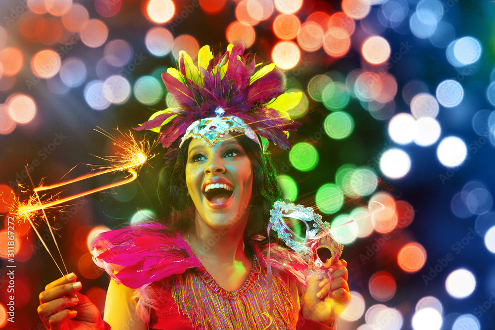 Beautiful young woman in carnival mask and stylish masquerade costume with feathers and sparklers in colorful bokeh on black background. Christmas, New Year, celebration. Festive time, dance, party. - obrazy, fototapety, plakaty 