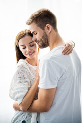 handsome man hugging attractive and smiling woman in apartment