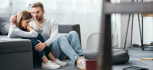 Wall Mural - panoramic shot of handsome man calming down sad woman in robbed apartment